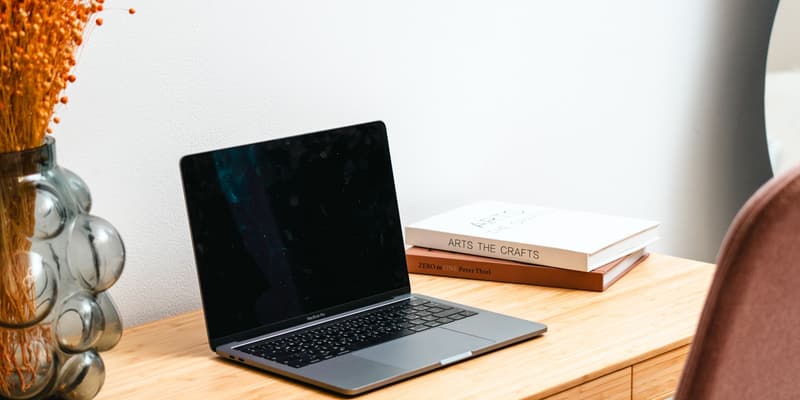 Laptop på ett ljust skrivbord i trä bredvid böcker och en vas