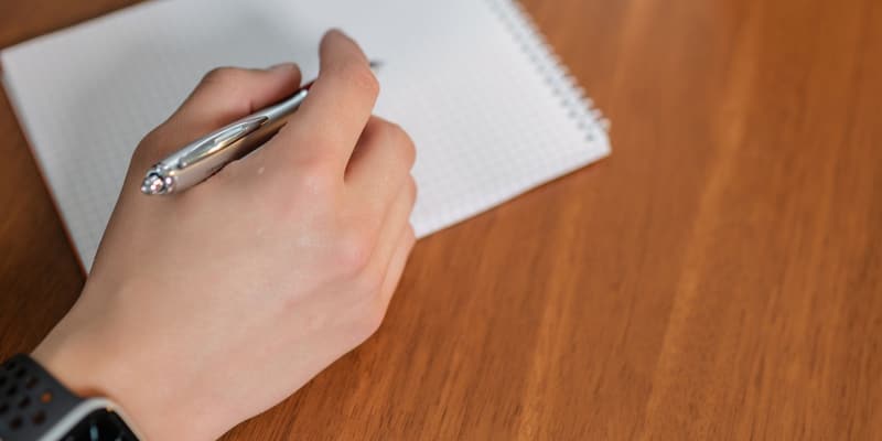 En hand som antecknar med penna i ett block på ett skrivbord